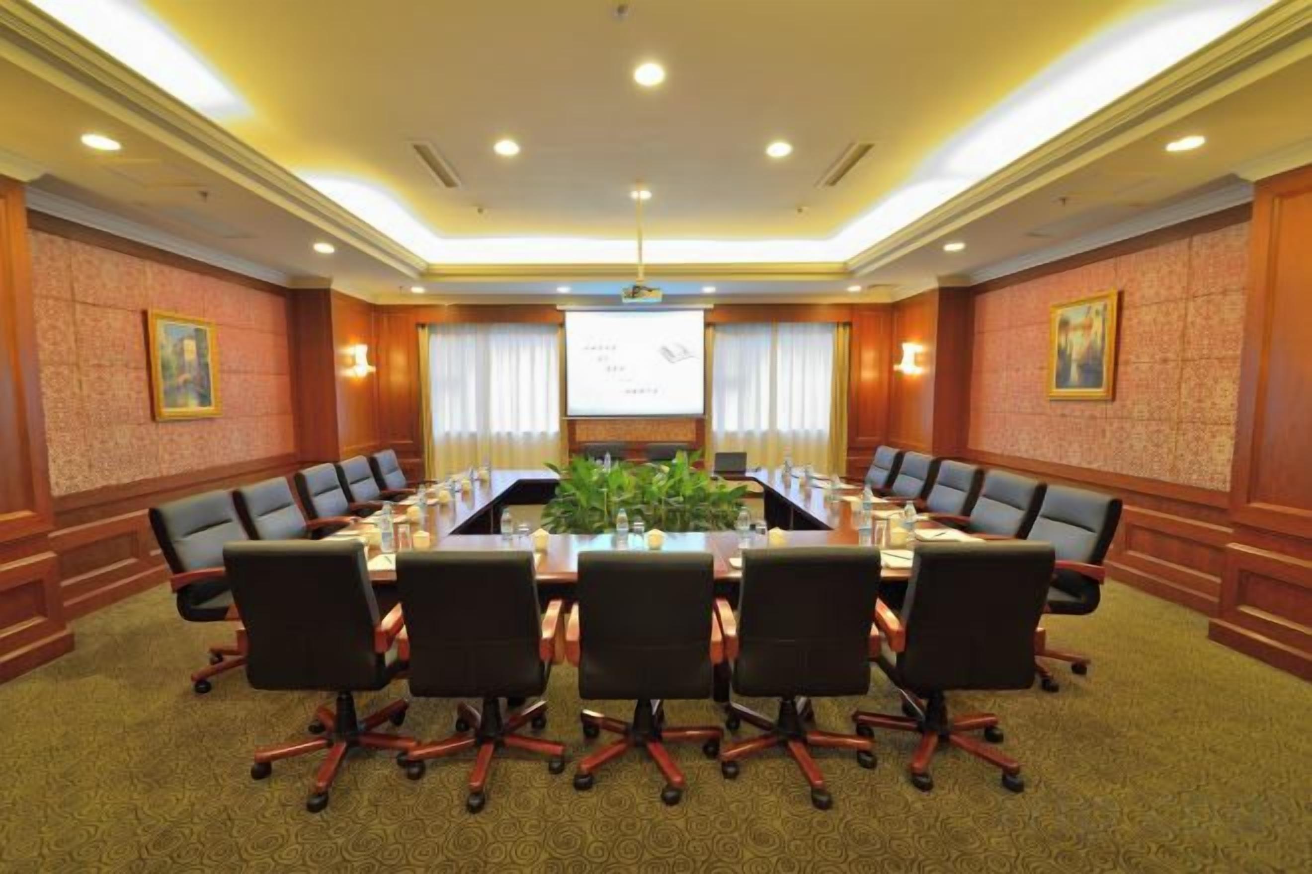 Un salón de conferencias con una larga mesa, varias sillas y una pantalla para proyector.