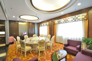 A hotel room with a dining table set for six, surrounded by chairs, a sofa, and a small round table with a decorative item. - Perfect International Hotel (Qidong)