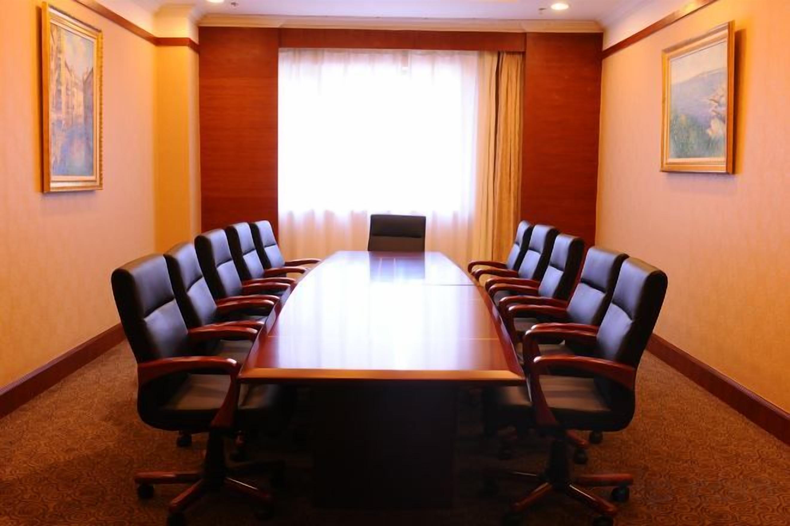 A conference room with a long table and multiple chairs, a window with curtains, and framed artwork on the walls.