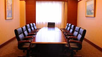 A conference room with a long table and multiple chairs, a window with curtains, and framed artwork on the walls.