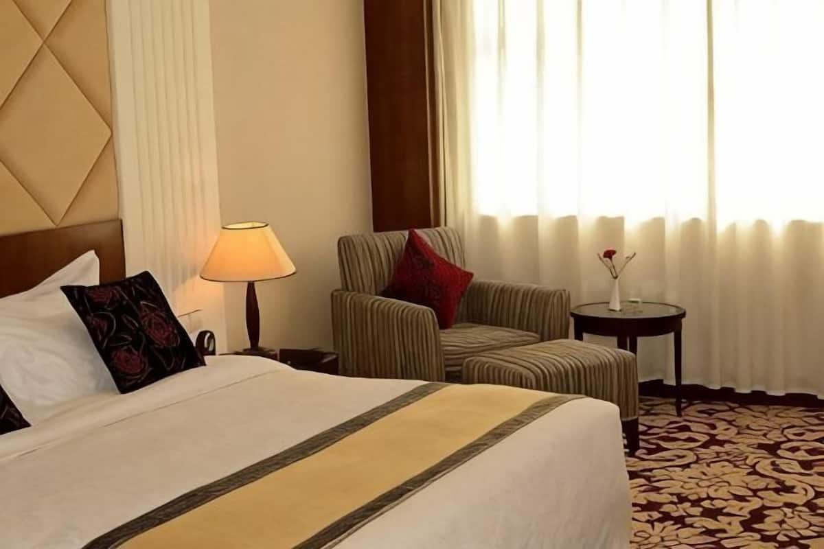 A hotel room with a large bed, a chair, a small table, and a window with curtains.