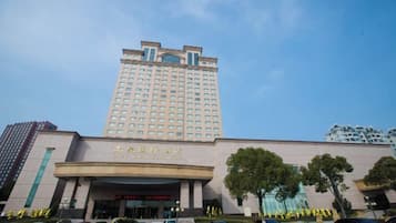 Un hotel de varios pisos con una entrada destacada y un edificio grande al fondo.