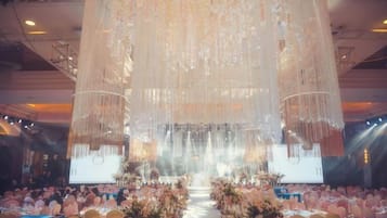 A banquet hall with tiered seating, a stage with a large screen, and hanging decorations.