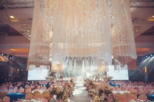 A banquet hall with tiered seating, a stage with a large screen, and hanging decorations.