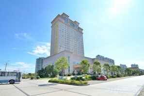 A multi-story hotel with a central courtyard, surrounded by greenery and a parking area. - Perfect International Hotel (Qidong)