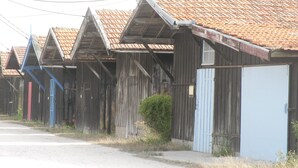 Una hilera de edificios rústicos de madera con techos a dos aguas y un camino de tierra al frente.