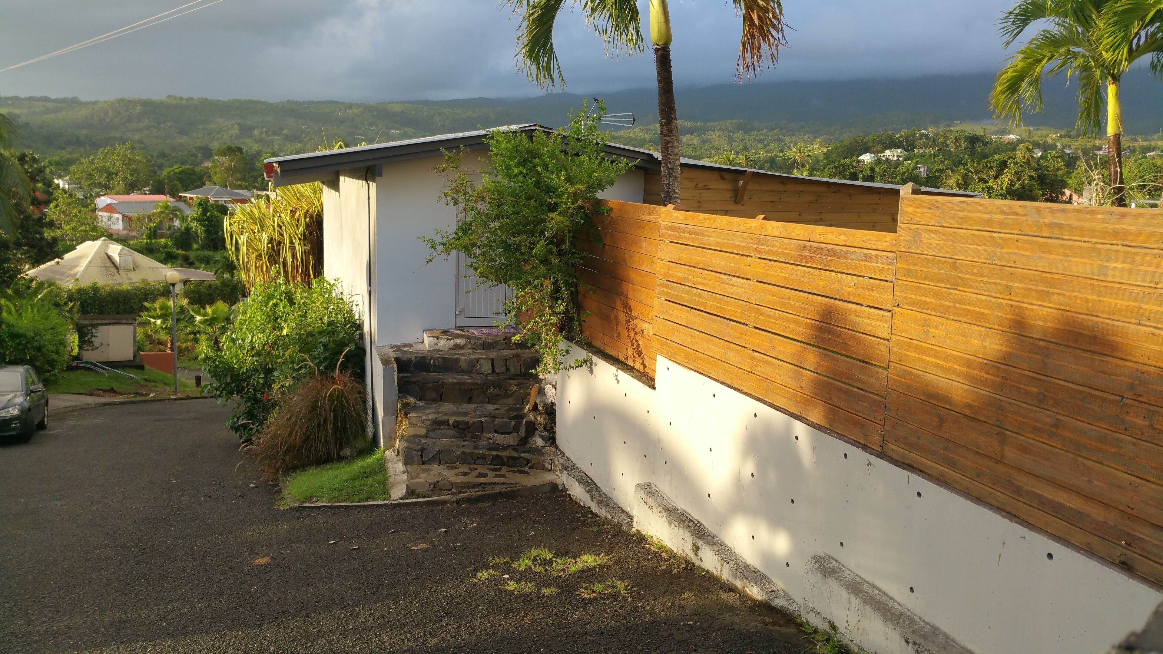A residential area with a wooden fence, a white wall, and a staircase leading to a house.