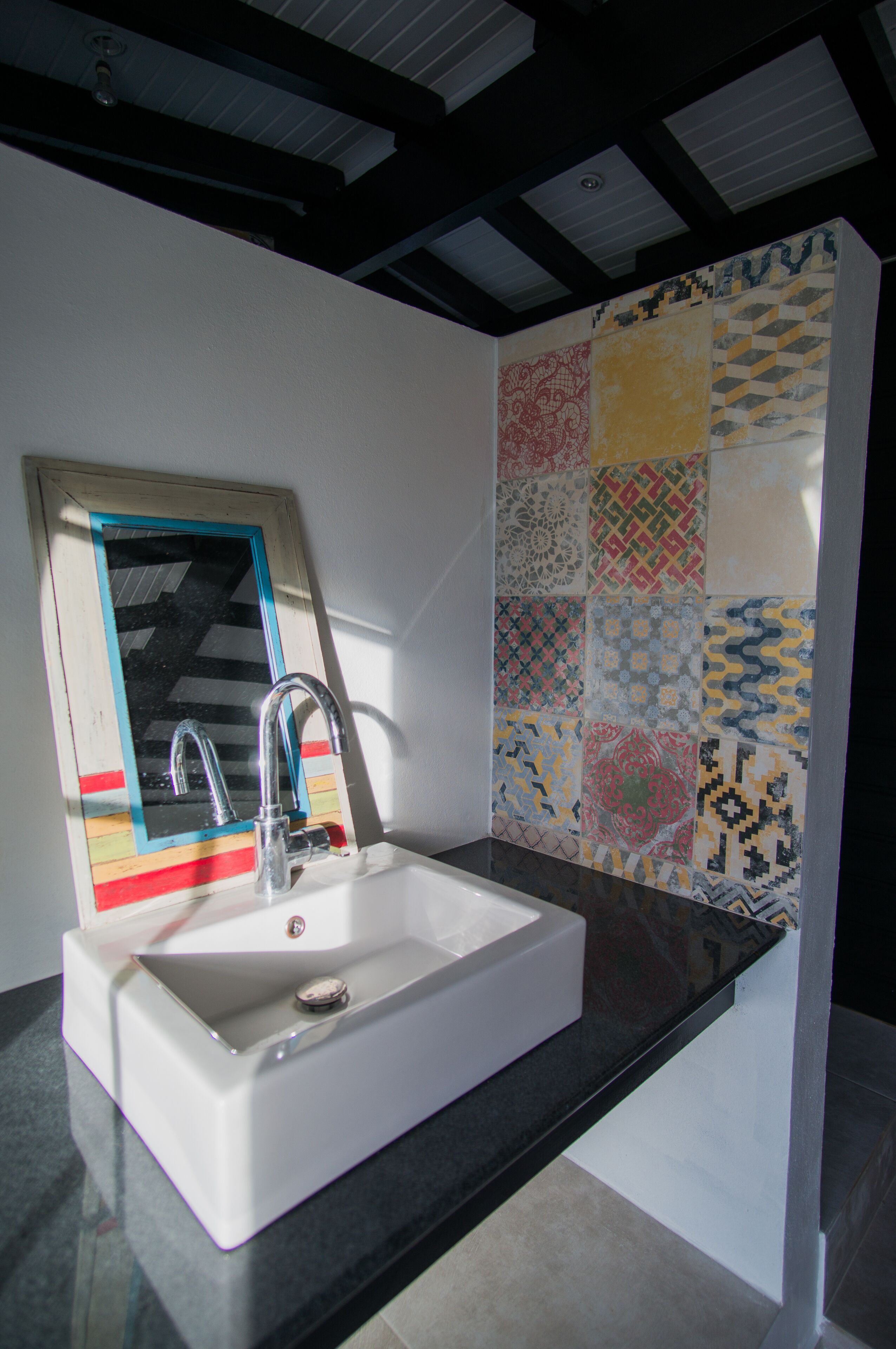 A bathroom with a white sink, a mirror, and a tiled wall with various patterns.