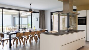 Una cocina moderna con una isla grande, una zona de comedor con sillas y una mesa, y ventanas amplias que ofrecen una vista.
