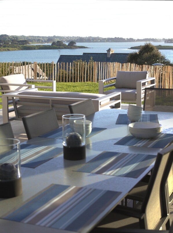 An outdoor dining area with a view of a lake, wooden deck, and a stone wall.