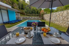 Une table à manger dressée pour le petit-déjeuner, avec vue sur une piscine et un mur en pierre.