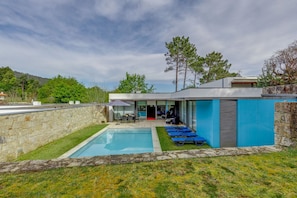 A modern house with a swimming pool, outdoor seating, and a stone wall.