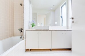 Une salle de bain moderne avec une baignoire, des meubles blancs, un lavabo et un miroir.