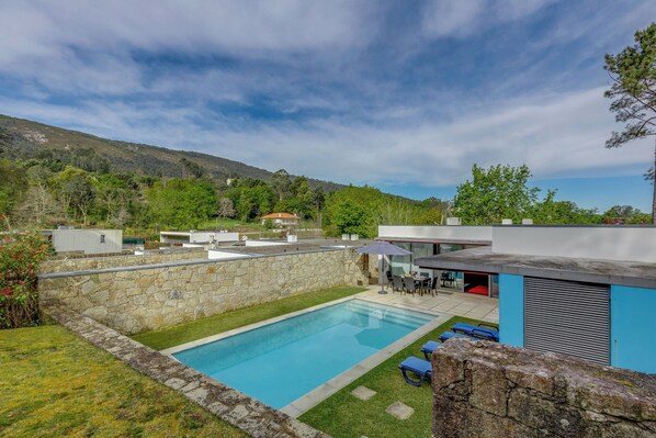 Un espace piscine extérieur moderne, agrémenté d’un mur en pierre, d’une piscine bleue et d’une terrasse avec des meubles d’extérieur.
