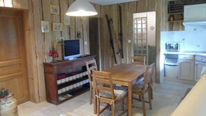 A dining area with a wooden table and chairs, a television on a wooden stand, and a kitchen area with a microwave and toaster.