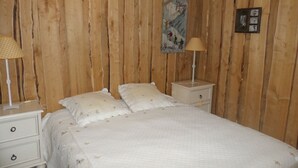 A bedroom with a wooden panel wall, a bed with white bedding, two bedside tables with lamps, and a small painting on the wall.
