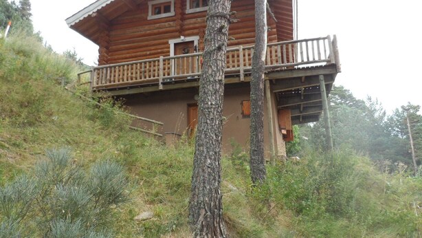 A wooden cabin with a balcony, surrounded by trees and vegetation.