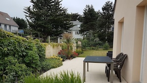 Une terrasse avec une table et des chaises, entourée d’une végétation luxuriante et d’un jardin.