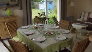 Une table à manger dressée pour six personnes, recouverte d’une nappe verte et entourée de chaises en bois.