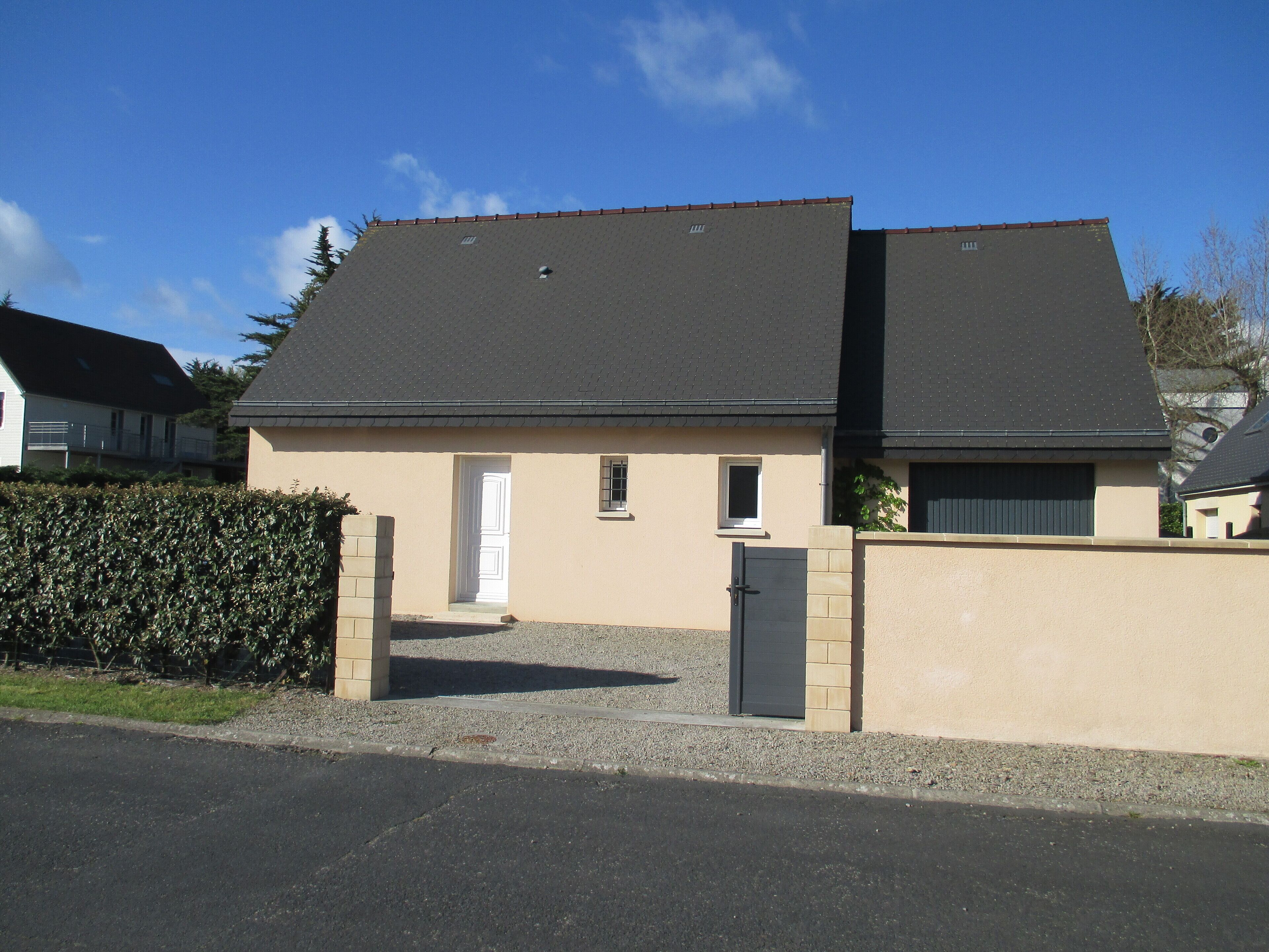 Une maison à deux étages, avec un toit sombre, des murs de couleur beige et une petite fenêtre.
