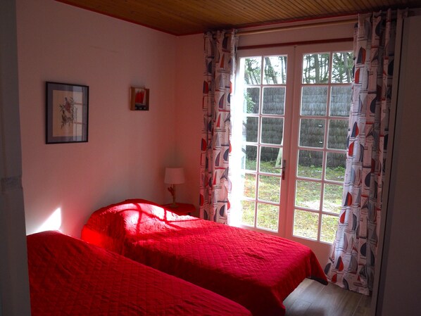 Una habitación con dos camas, una ventana con cortinas, un cuadro en la pared y una lámpara en una mesita de noche.