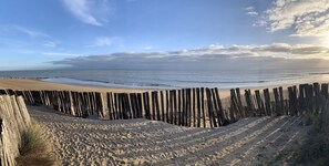 Una playa arenosa con una cerca de madera en primer plano y un mar tranquilo al fondo.