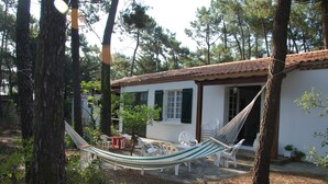 Un espacio al aire libre rústico con una hamaca, sillas blancas y una pequeña mesa.