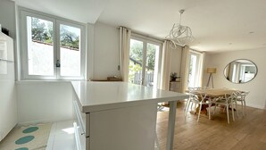 Een ruime keuken met een groot kookeiland, een eethoek met een houten tafel en stoelen, en grote ramen die zorgen voor natuurlijk licht.