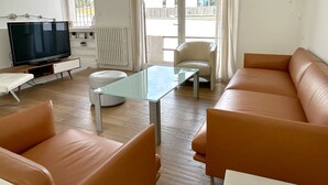 Een woonkamer met een glazen salontafel, leren banken, een televisie en uitzicht door grote ramen.