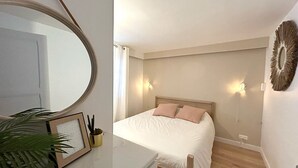 Een slaapkamer met een bed, bedlampen, een spiegel, een lijst met een afbeelding en een potplant.