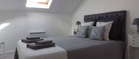 Une chambre avec un plafond en pente, un puits de lumière, un lit avec une literie grise, deux tables de chevet avec des lampes et un appareil de climatisation blanc.
