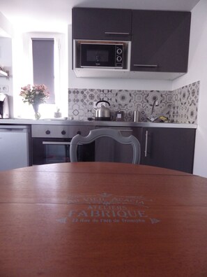 A kitchen with dark cabinets, a microwave, a kettle, and a dining table with a logo.