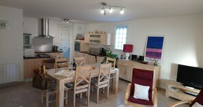 A compact kitchen with a microwave, stove, and cabinets. There is a dining table with chairs, a TV, and a red chair with a white cushion.