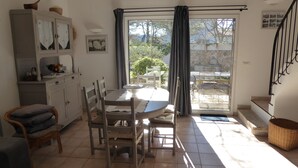 A dining area with a table and chairs, a cabinet with glass doors, a wicker basket, and a view through a glass door to an outdoor patio. - The Cabanon (Saint-Saturnin-Lès-Apt)