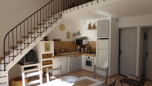 A kitchen with white cabinets, a microwave, a stove, and a sink. There is a staircase with a black railing leading to an upper level. - The Cabanon (Saint-Saturnin-Lès-Apt)