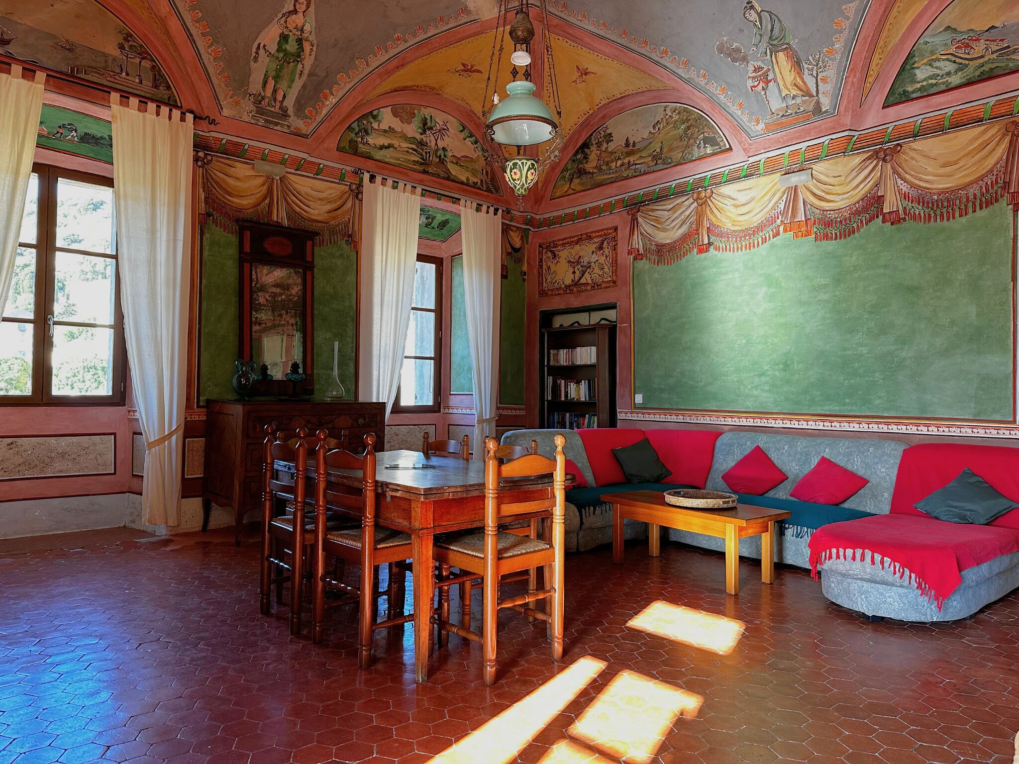 A room with a wooden dining table, chairs, a sofa, and a green chalkboard wall.