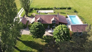 A large house with a swimming pool, surrounded by a well-maintained lawn and trees.