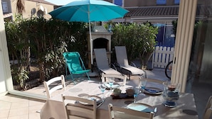 An outdoor patio with a table set for dining, surrounded by chairs, and an umbrella providing shade. - PORTIRAGNES BEACH. HOUSE T3 IN RESIDENCE WITH POOL 700m FROM THE BEACH. (Portiragnes)