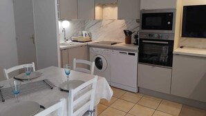 A compact kitchen with a washing machine, oven, microwave, and a dining area with a table set for two. - PORTIRAGNES BEACH. HOUSE T3 IN RESIDENCE WITH POOL 700m FROM THE BEACH. (Portiragnes)