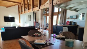 Un coin repas avec une table en bois dressée pour deux personnes, un canapé et une cuisine en arrière-plan.
