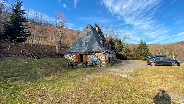 Une maison en pierre avec un toit en pente, une cheminée et une voiture garée devant.