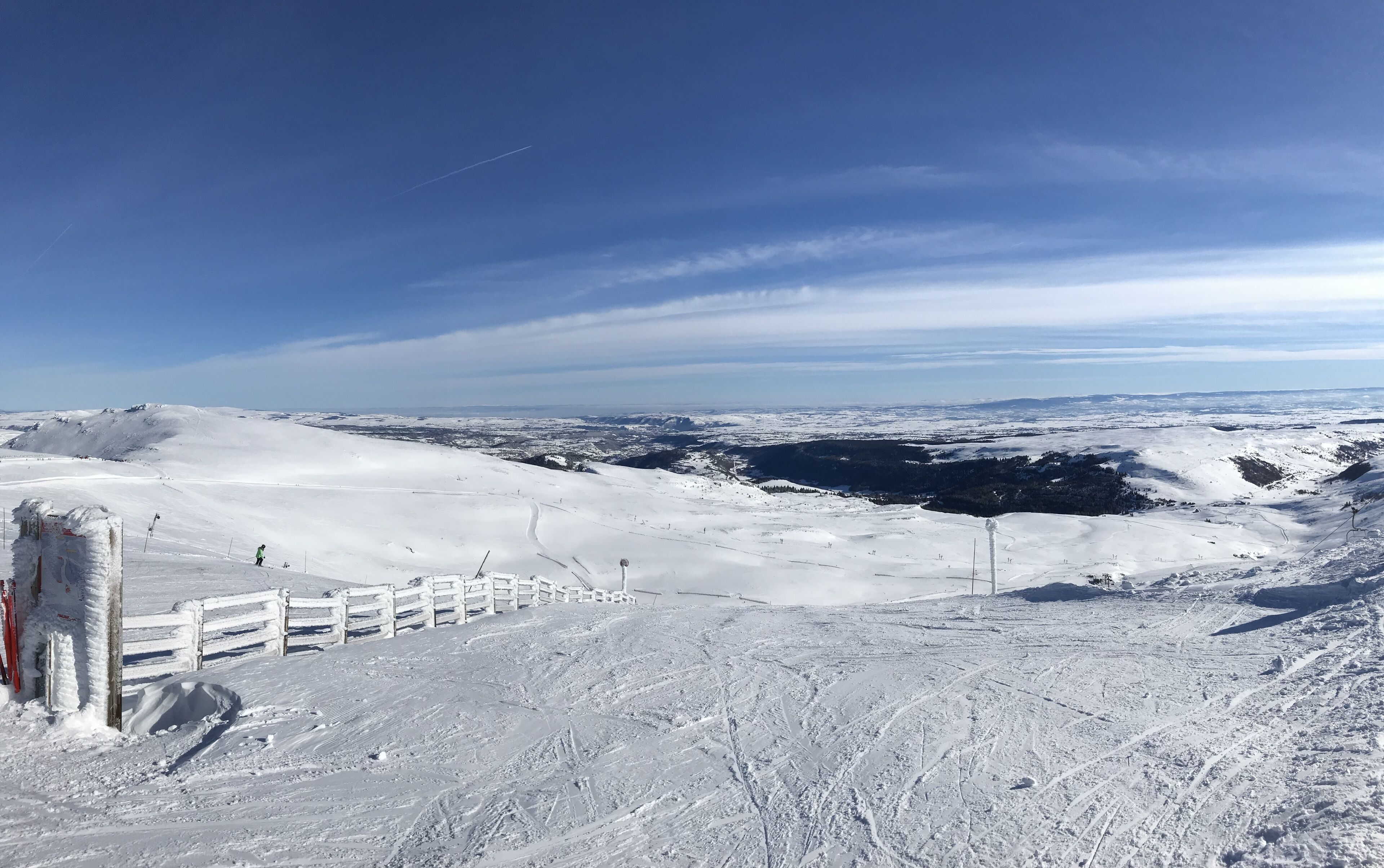 Paesaggio innevato con cielo sereno, una recinzione in legno e una vista lontana di una valle.