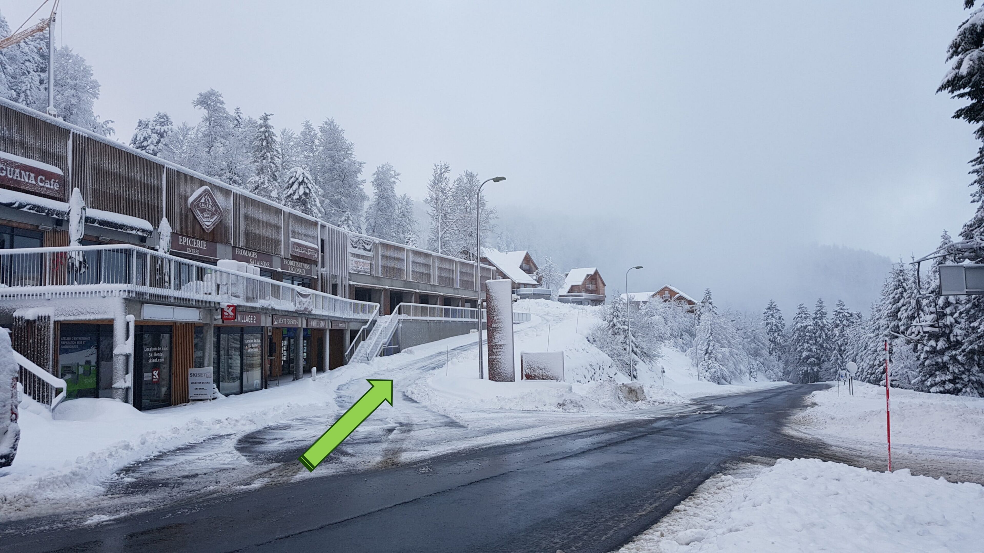 A snow-covered street with buildings, including a café and shops.