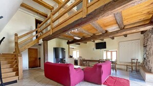 Un vaste espace de vie doté d’un haut plafond en bois, d’un canapé rouge, d’un escalier en bois et d’un mur en pierre.