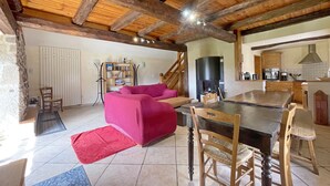 Un vaste espace de vie avec un canapé rouge, une table à manger en bois et des chaises. On aperçoit, au fond, une cuisine avec des meubles en bois et une cheminée.