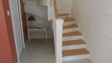 Eine Treppe mit Holzstufen und weißen Wänden führt zu einer Empore mit einem kleinen Tisch und einer Lampe.
