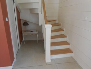 Una escalera de madera con paredes blancas que lleva a un rellano con una mesa pequeña y una lámpara.