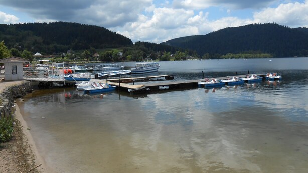 A marina with boats docked, a small building, and a lake surrounded by hills.