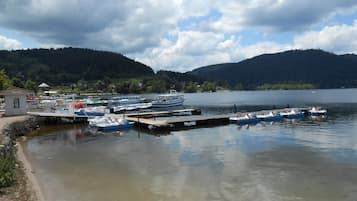 Ein Yachthafen mit vertäuten Booten, ein kleines Gebäude und ein See, der von Hügeln umgeben ist.