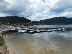 Un port de plaisance avec des bateaux amarrés, un petit bâtiment et un lac entouré de collines.